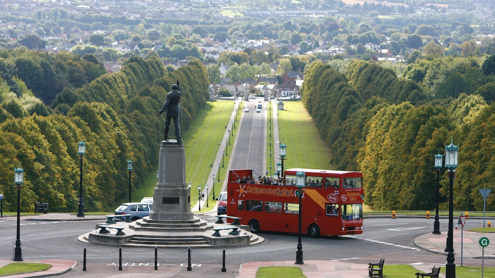 Hop on hop off double decker bus driving past a park in Belfast