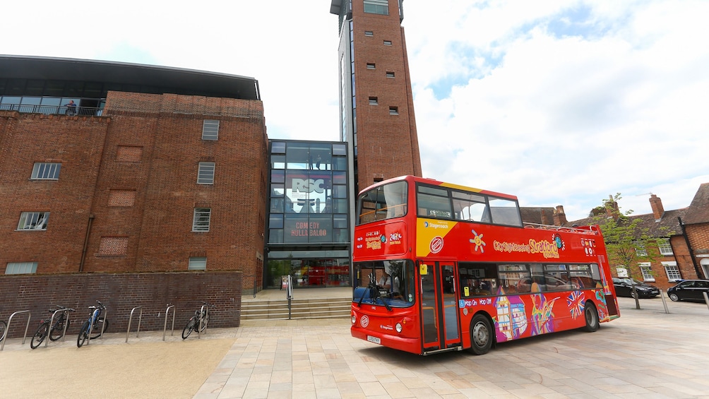 A hop on hop off bus driving past a modern building in Stratford upon avon