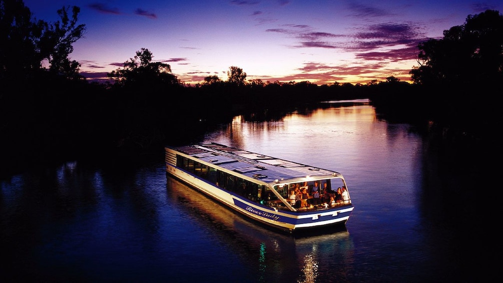 A cruise boat sailing up a river in perth at sunset