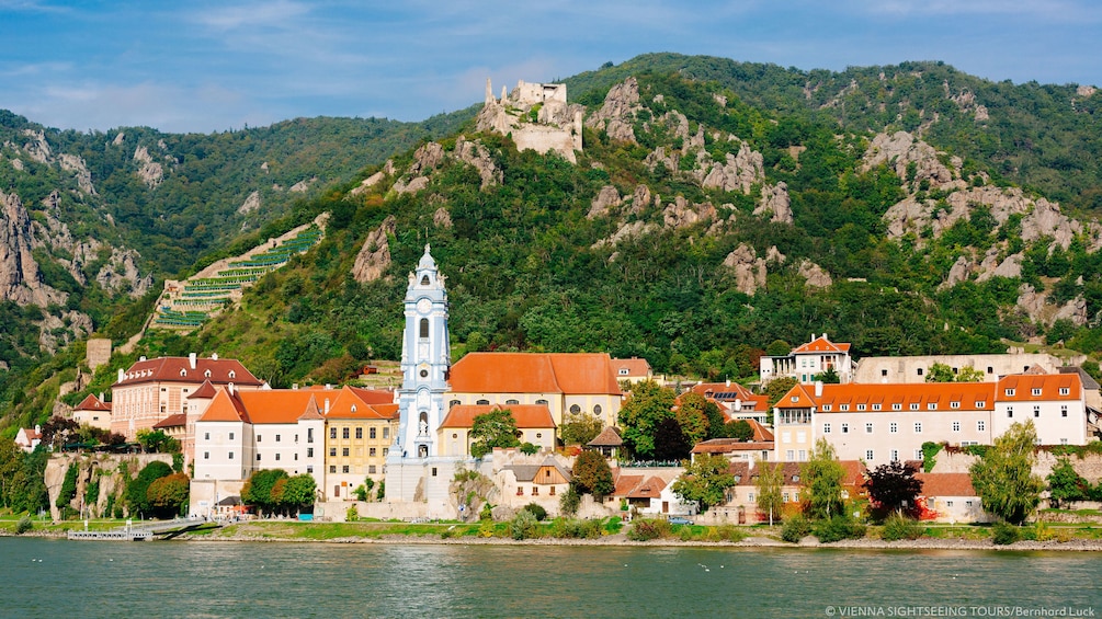 Bell tower stands above other buildings along river shore in Wachau