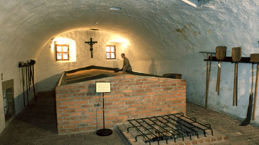 Staged scene depicting a glassblower gathering sand at a chapel in Prague