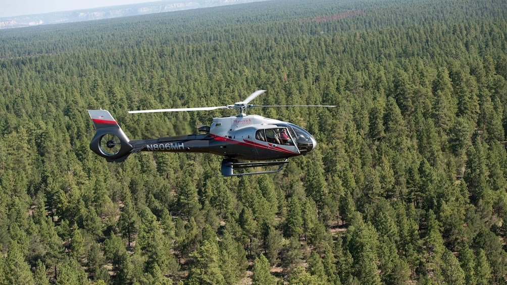 Helicopter flying above green trees in the Grand Canyon area
