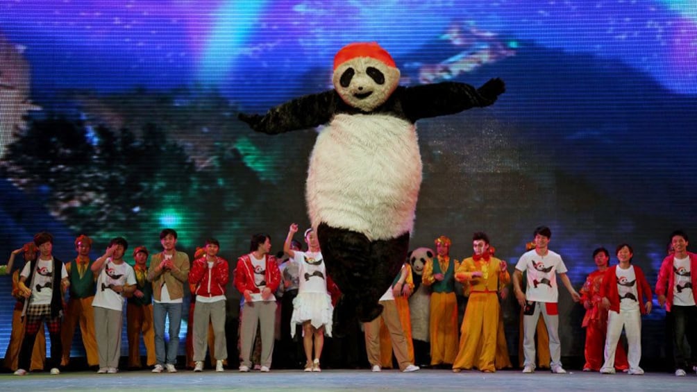 Show item 3 of 10. Performer in panda suit jumping on stage in Beijing