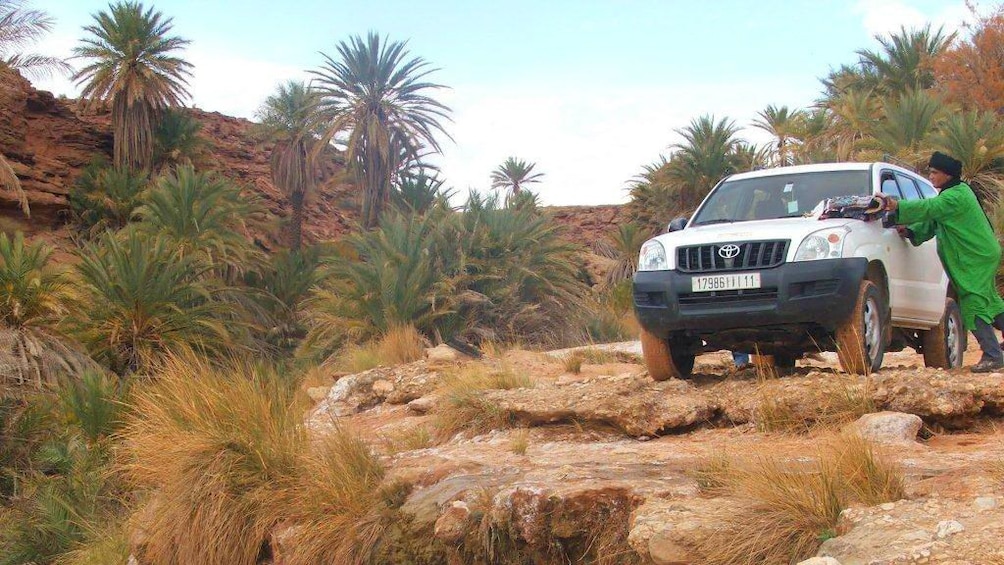 Jeep parked on a cliff surrounded by red rocks and palm trees in Marrakech