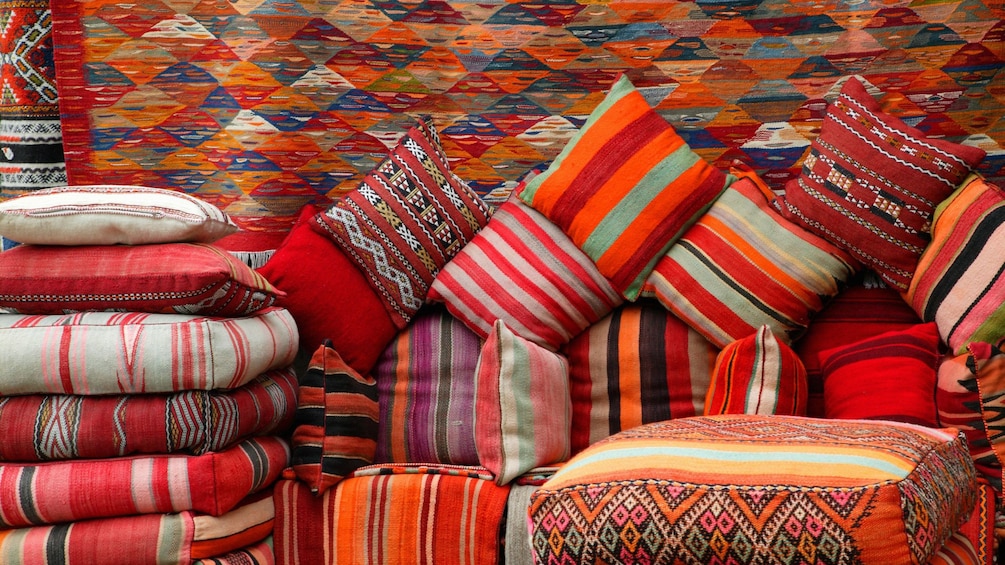 Piles of colorful cushions and hanging rugs at a market in Ouarzazate