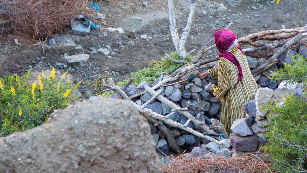 Local woman in colorful robes placing rocks on a hill near Marrakech