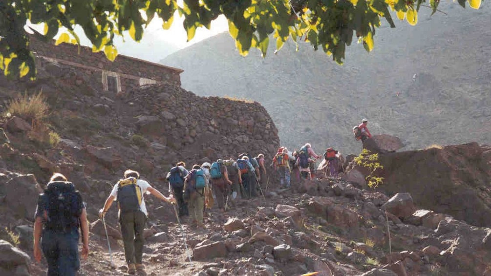 Atlas Mountain hiking group on a trail near a stone house in Marrakech