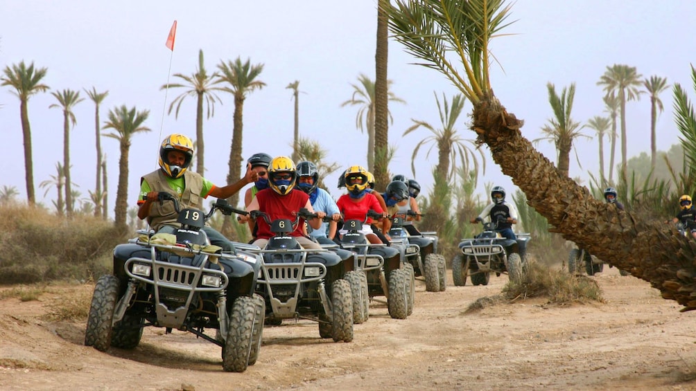 Quad-biking group on a dirt road lined with palm trees in Marrakech