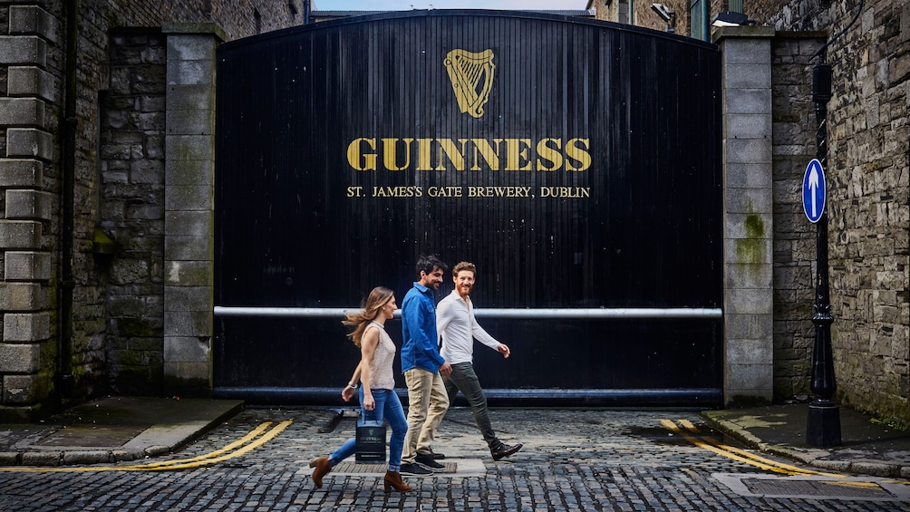 Show item 4 of 9. Three people walking in front of Guinness Brewery