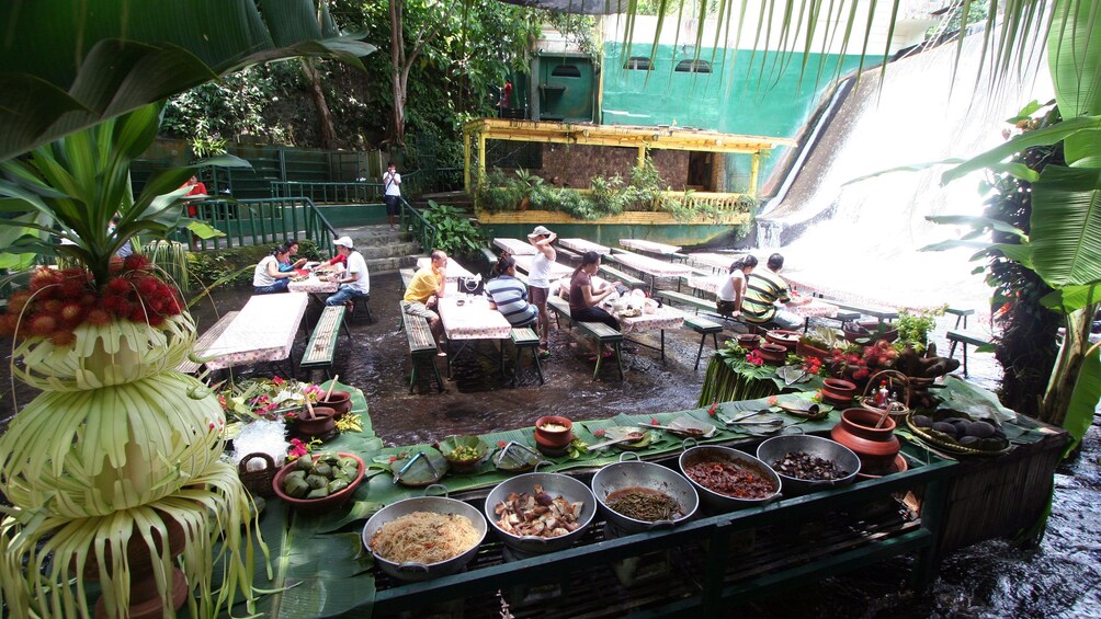 Bowls of prepared food and guests dining at the base of a waterfall at Villa Escudero Plantations in San Pablo City, Philippines