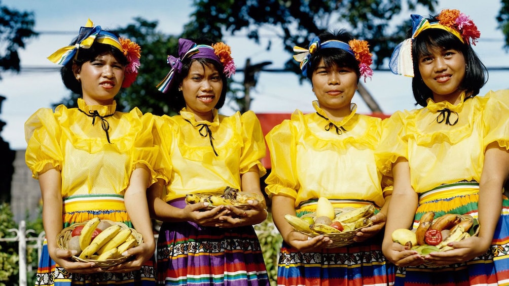 Young women in colorful costumes holding baskets of fruit in Manila