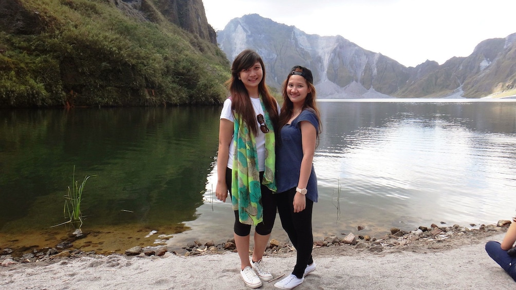 Pair of young women standing on the lakeshore with Mount Pinatubo in the background in the Philippines