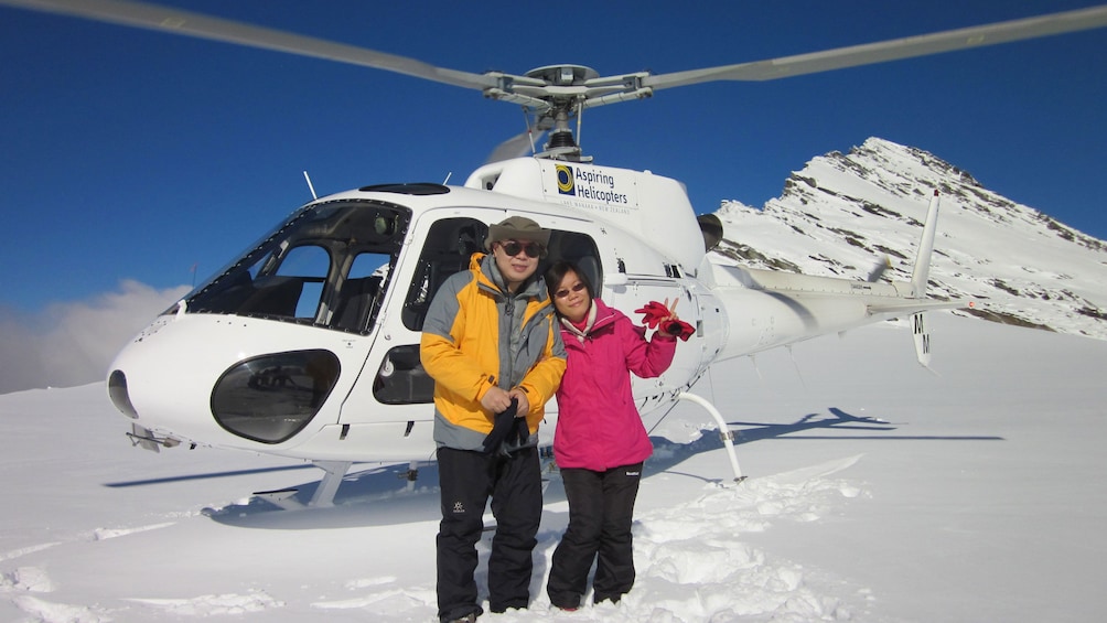 Couple in front of a Helicopter on a snowy mountain top