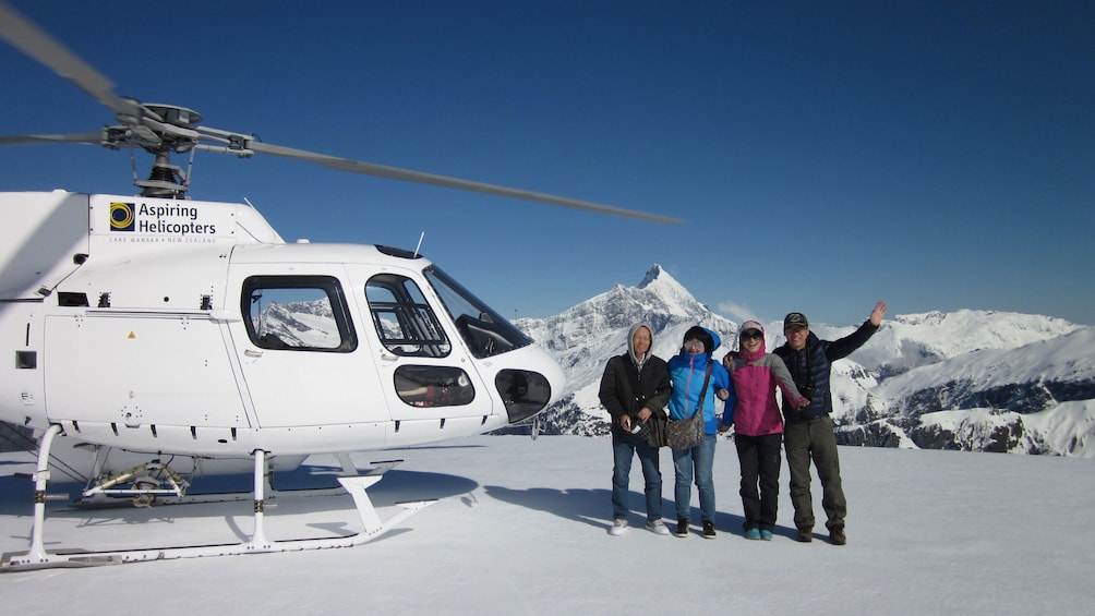 Group stands next to Helicopter on snowy mountain top