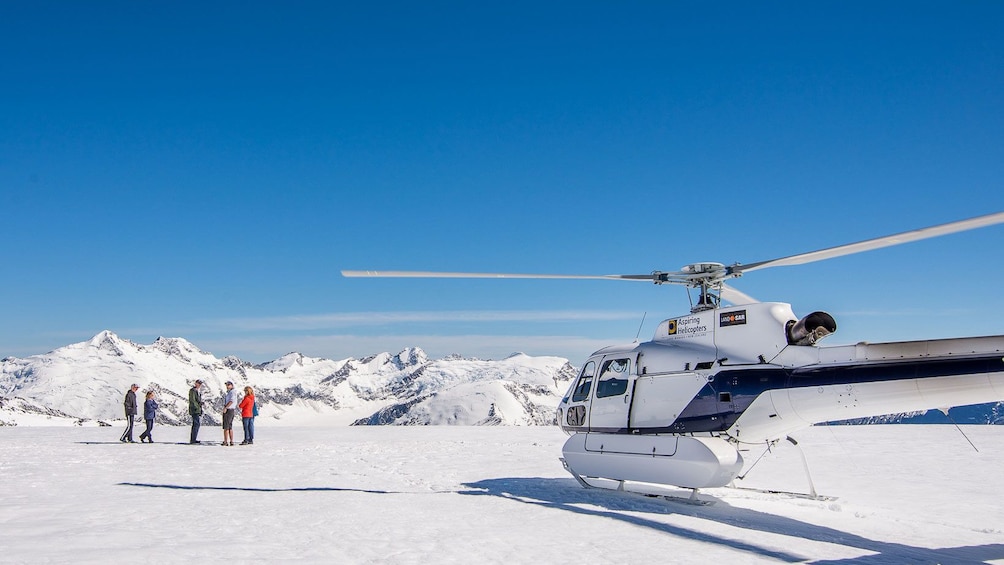 Tour group on a snowy mountain top next to Helicopter