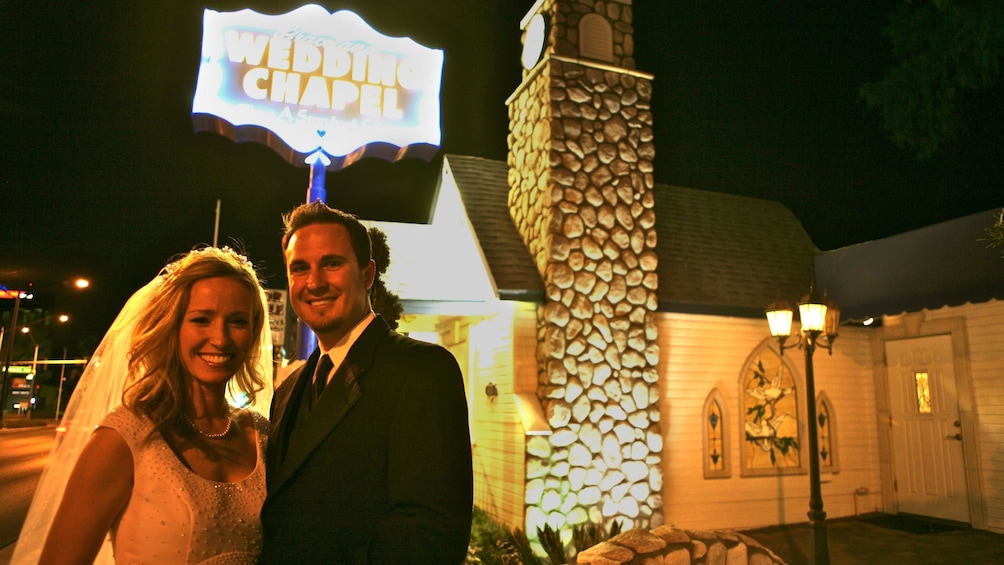 Happy bride and groom pose in front of the wedding chapel in celebration of their new marriage
