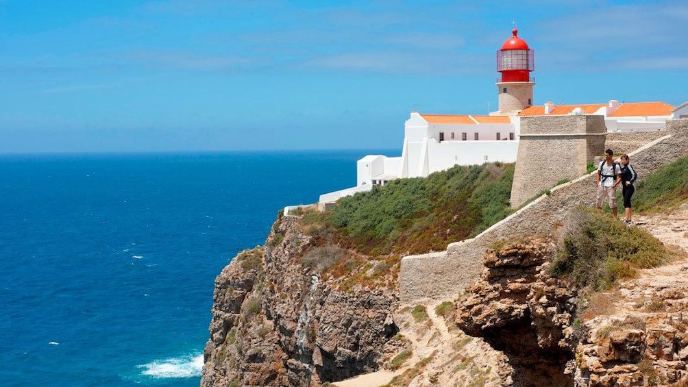 Couple standing on the rocky coastal cliffs with Ponta da Piedade lighthouse in the background in Lagos