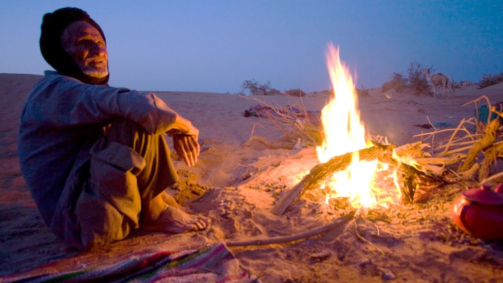 Berber man sitting by a campfire in the desert in 