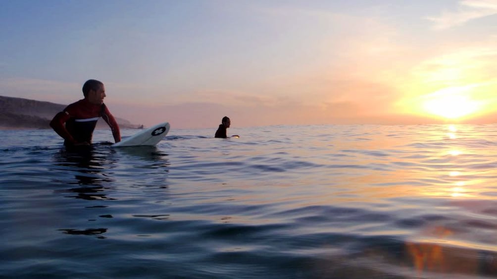 Pair of surfers sitting on their surfboards in the water at sunset in Agadir