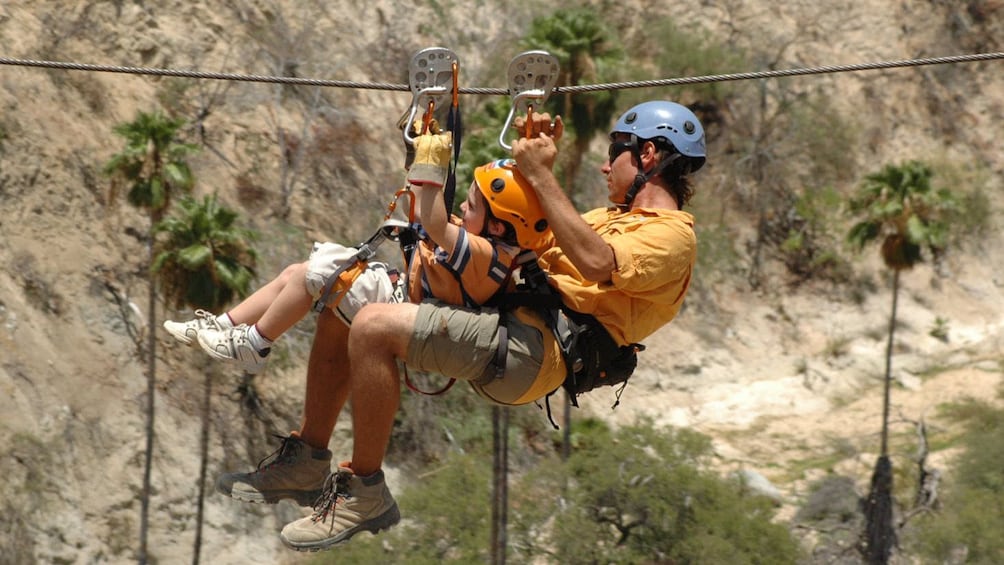 a man and young boy zip lining across the ground in Los Cabos