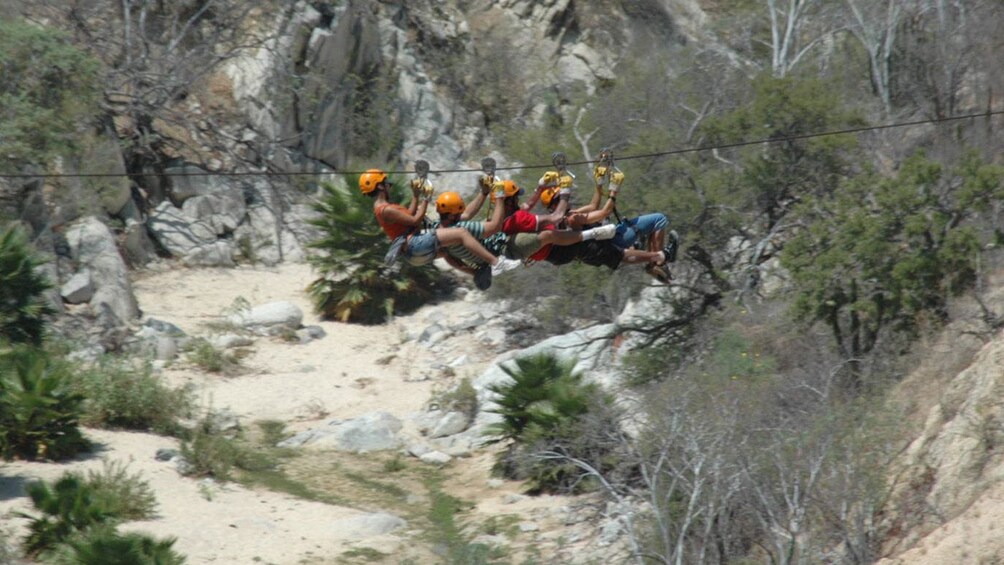 group of four people zip lining across the ground in Los Cabos