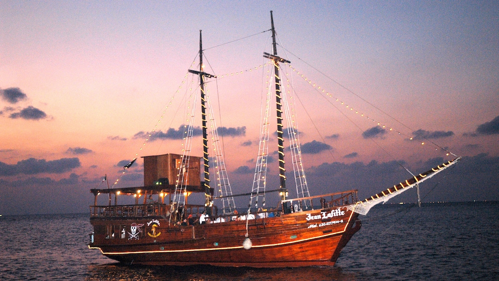 Show item 1 of 5. Illuminated pirate ship on the water at sunset in Cozumel