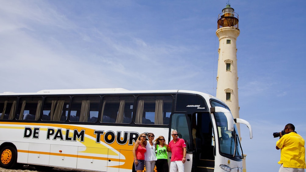 Guide takes group photo in front of tour bus with lighthouse in background