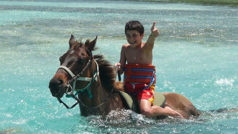 boy horse back swimming in the ocean along the jamaican coast 