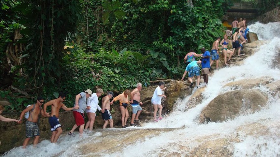 People hiking up a waterfall holding hand in Jamaica