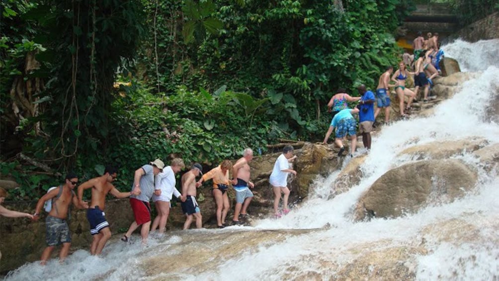 People hiking up a waterfall holding hand in Jamaica