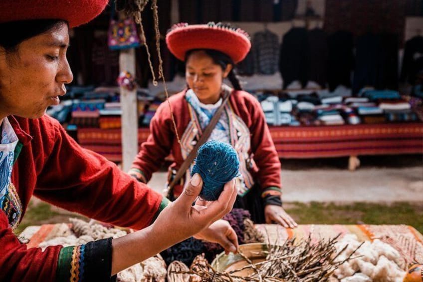 In Chincheros, Peru, a woman wearing traditional dress holds aloft a ball of yarn.
