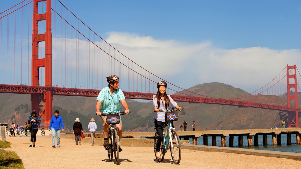 Two people riding a bike next to the Golden Gate Bridge
