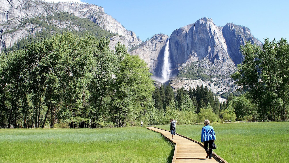 People walking on Sentinel Meadow boardwalk with waterfall in the distance at Yosemite National Park