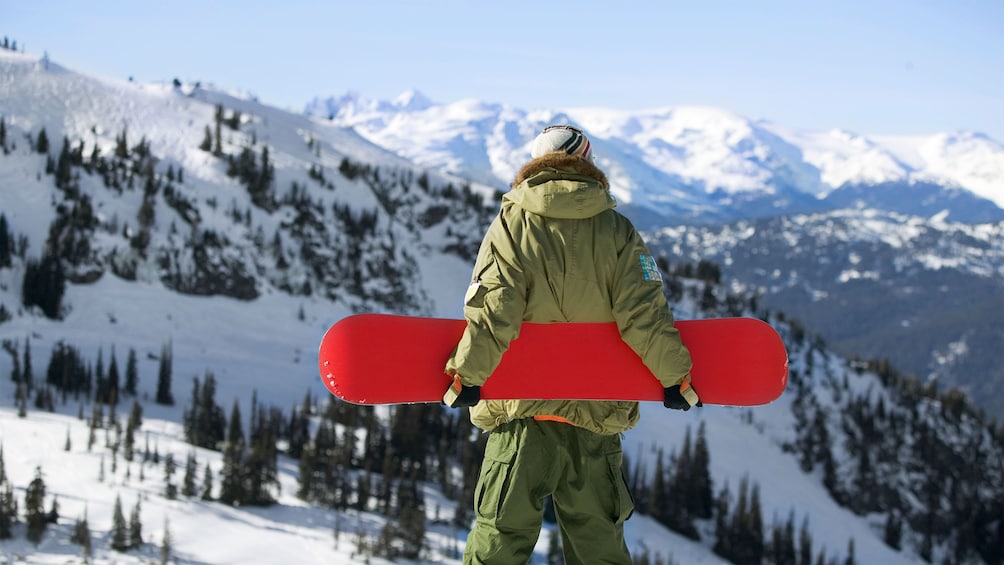 Man holding snowboard and looking out at the mountains in Park City