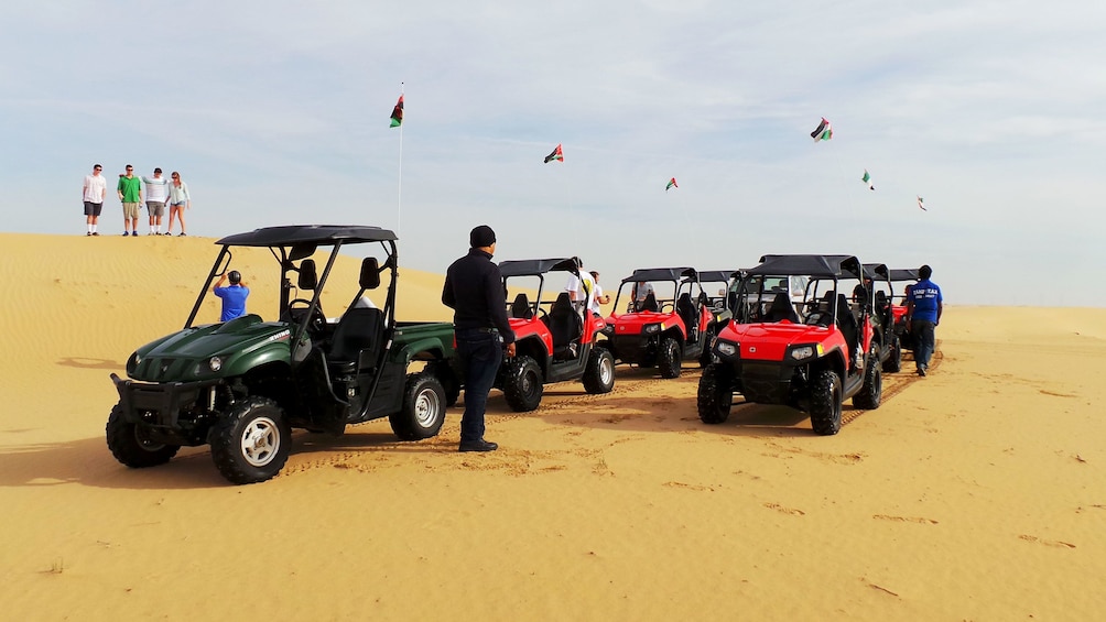 people walk around sand buggies parked on sand  dunes.