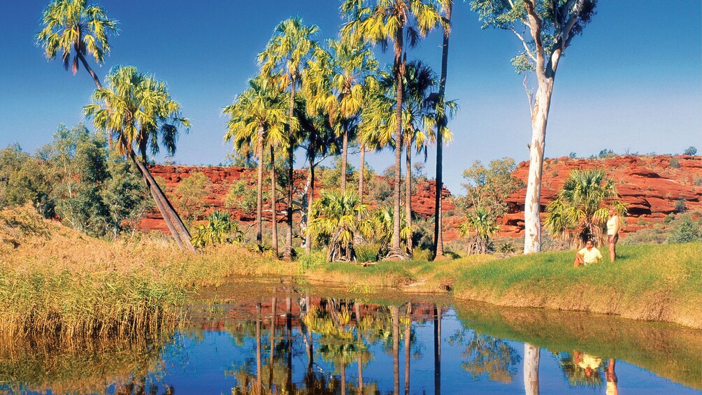 Couple relaxing near a pond with red rocks in the background in Palm Valley