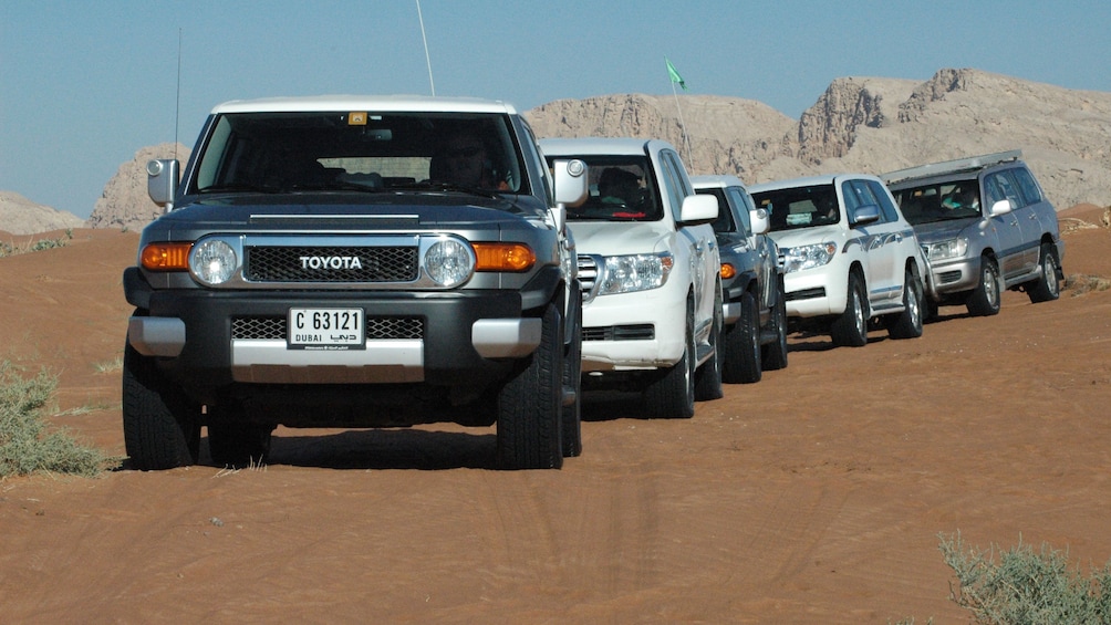 five SUVs driving on sandy ground in Abu Dhabi