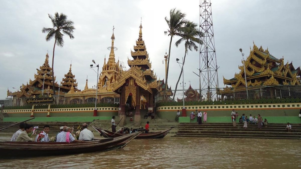 Passengers arrive at a temple in a wooden boat on the river in Syriam