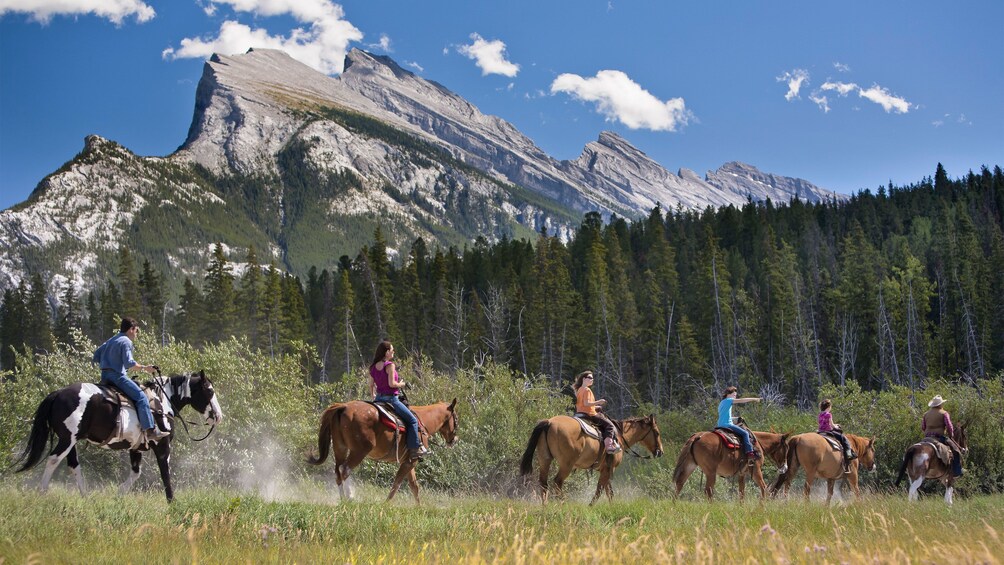 Tourists trek through Banff National Park on horseback with the Canadian Rockies in the background