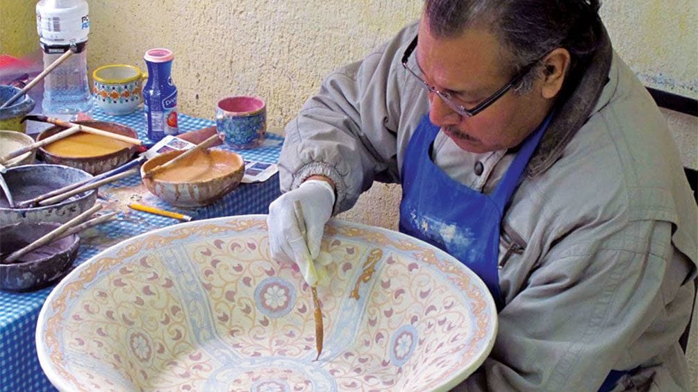 Man hand painting an elaborate design on a bowl in Puebla