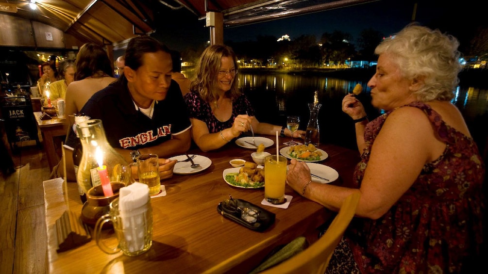 Close view of a family enjoying dinner aboard the Ping River Dinner Cruise in Chiang Mai with the scenic view of the water at night 