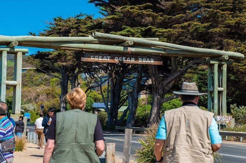 Khaki-clad visitors walk towards a Great Ocean Road sign in Australia.