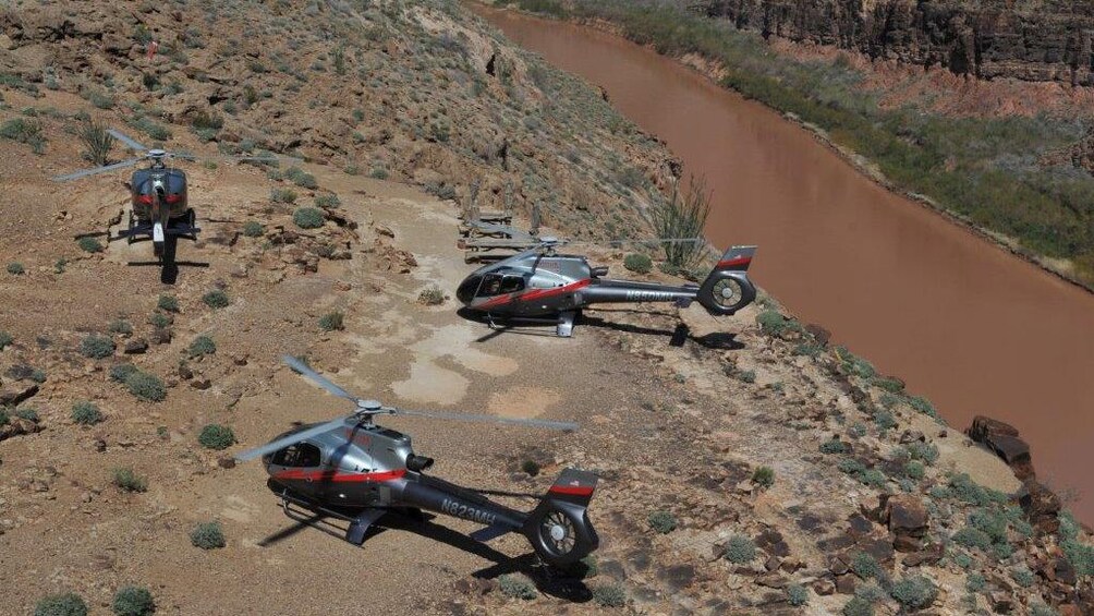 Three parked helicopters next to the Colorado river in the Grand Canyon