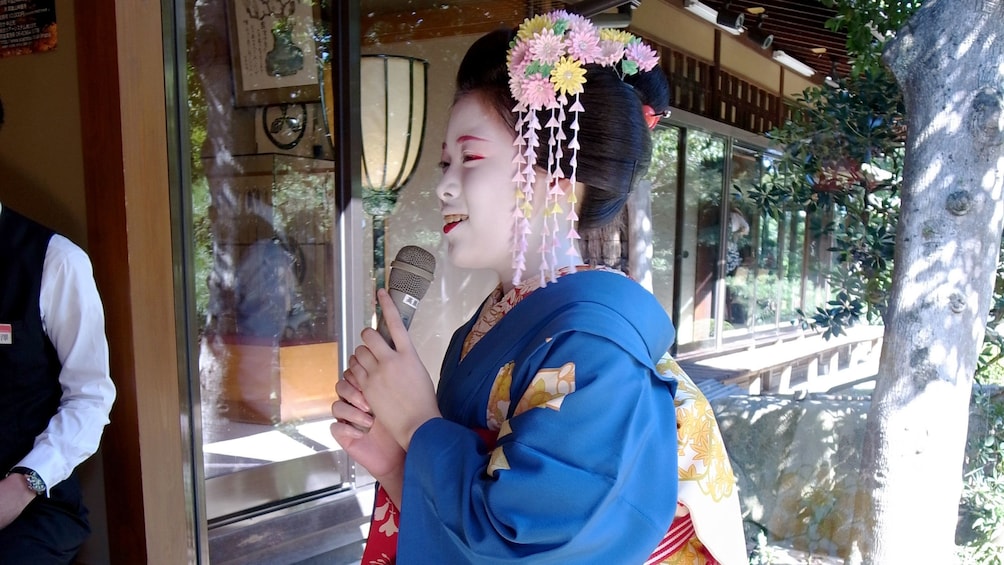 Show item 1 of 5. Woman in traditional outfit speaking on a microphone in Japan