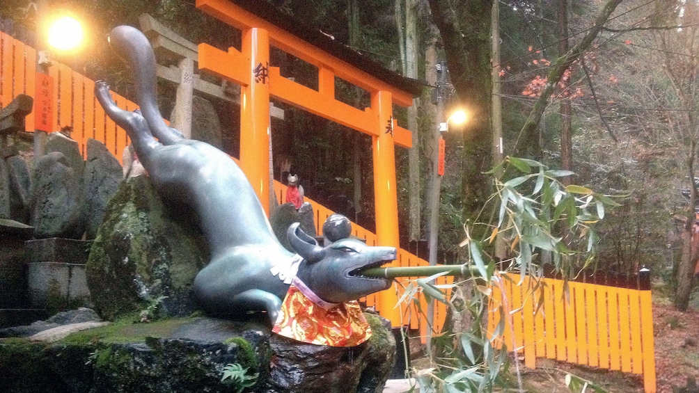 Show item 4 of 5. A Foz sculpture sits beside a torii gate at the entrance to Fushimi Inari shrine in Kyoto