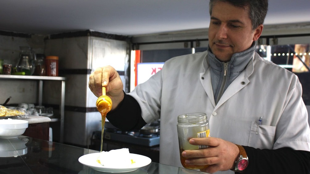 A chef preparing a food dish as he pours honey on to a plate
