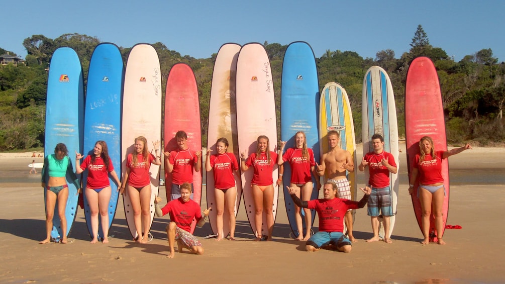 Pleasant group of surfers with surf boards behind them on Byron Bay beach.
