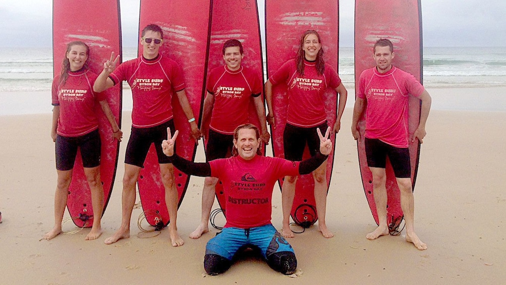 Happy group of student surfers with instructor on Byron Bay beach.
