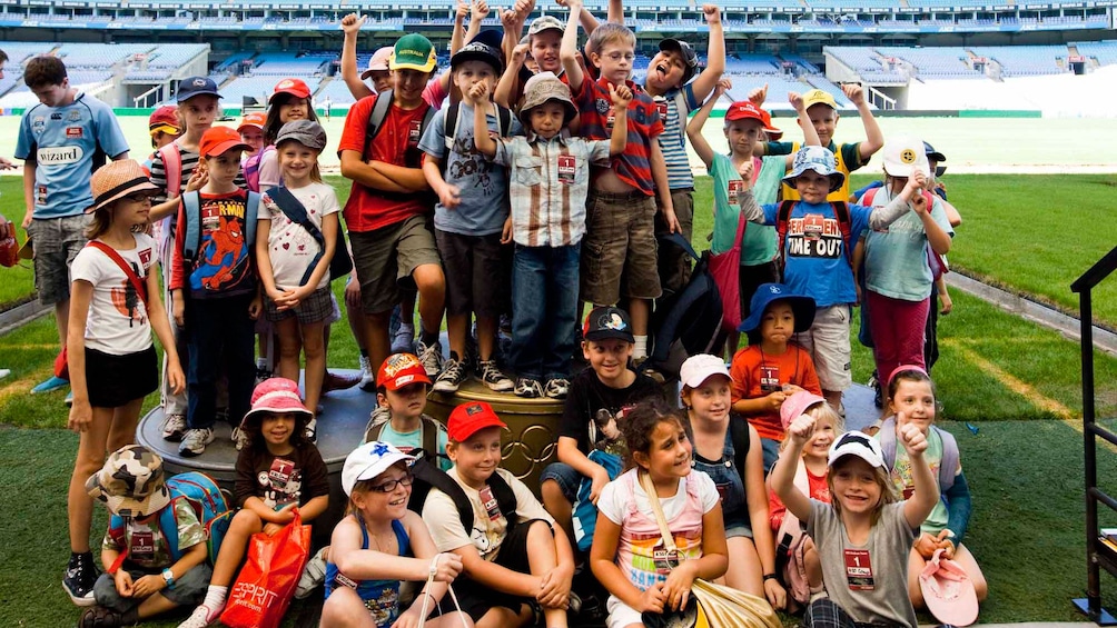 Show item 5 of 5. large group of children huddled together for photo op in stadium in Canberra