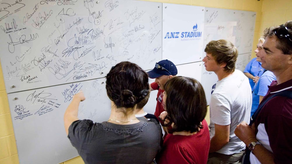 Show item 4 of 5. group of tourist looking at athlete signatures on white board in Stadium in Canberra